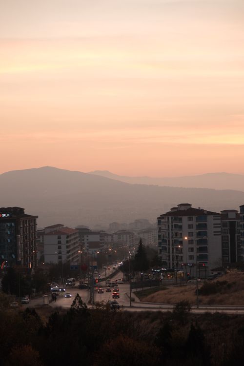 Free Urban landscape at sunset with city lights and distant mountains creating a serene horizon. Stock Photo