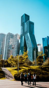 Dramatic cityscape with futuristic skyscrapers and a park under a clear blue sky.