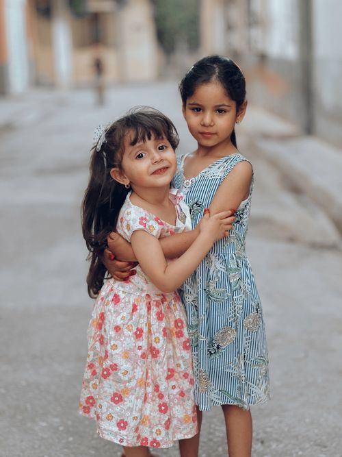 Free Heartwarming photo of two young girls hugging on a quiet urban street, capturing friendship and innocence. Stock Photo