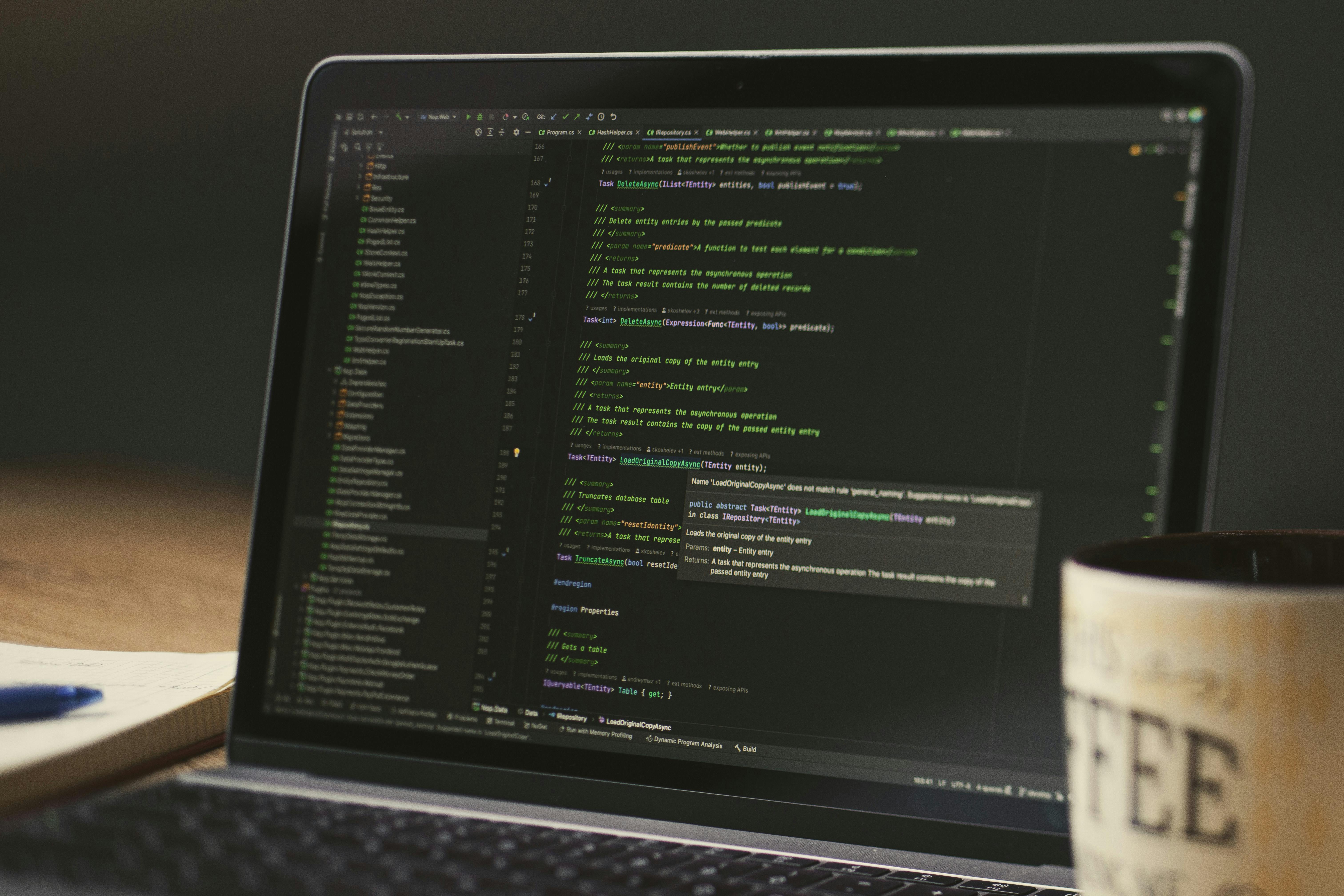Free A close-up of a laptop displaying code in a dimly lit room with a coffee mug nearby. Stock Photo