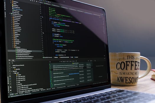 Close-up of laptop with coding software and a motivational coffee mug on a desk.