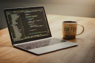 Open Laptop with Coding on Screen and Coffee Mug