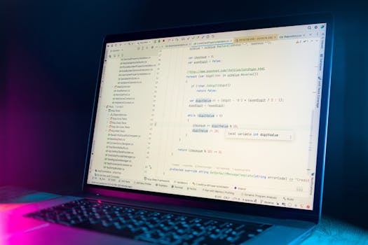 A laptop screen showing a code editor with visible programming code in a dimly lit environment.