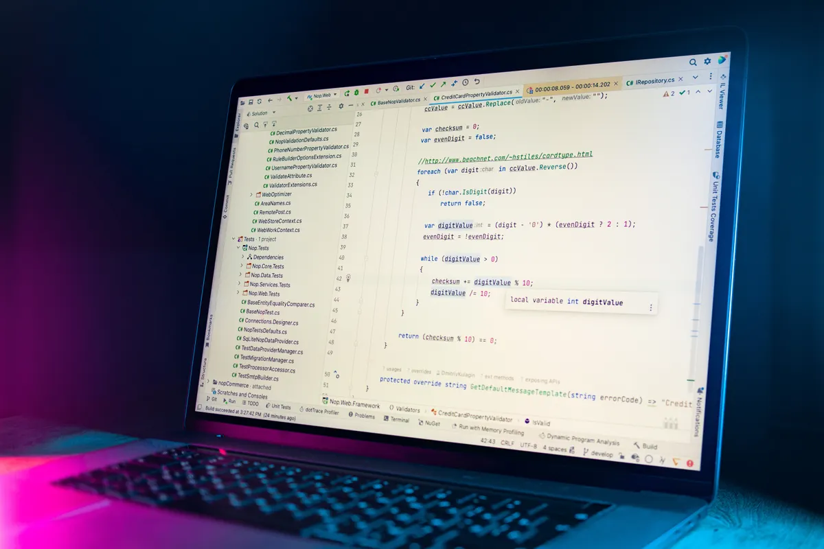 A laptop running a code editor filled with programming code in a dimly lit room.