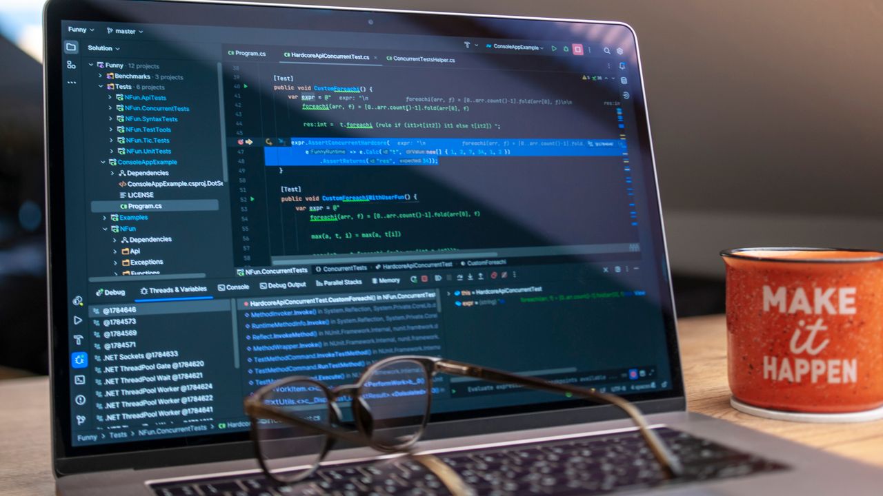 A laptop displaying code editor with a motivational mug that reads 'Make It Happen' on a workspace.