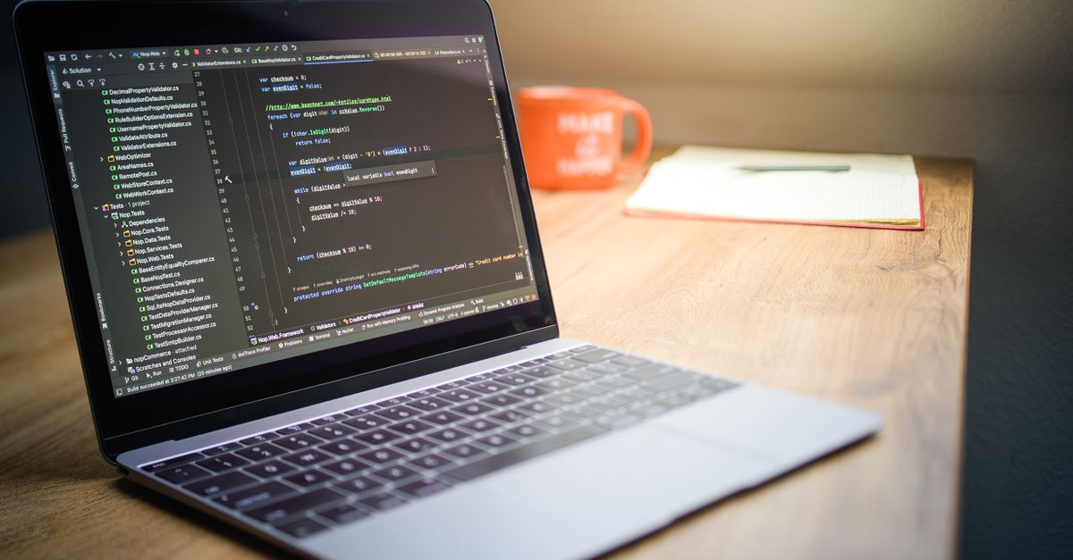 Laptop showcasing code on a desk with a notebook and mug, emphasizing a modern workspace setting.