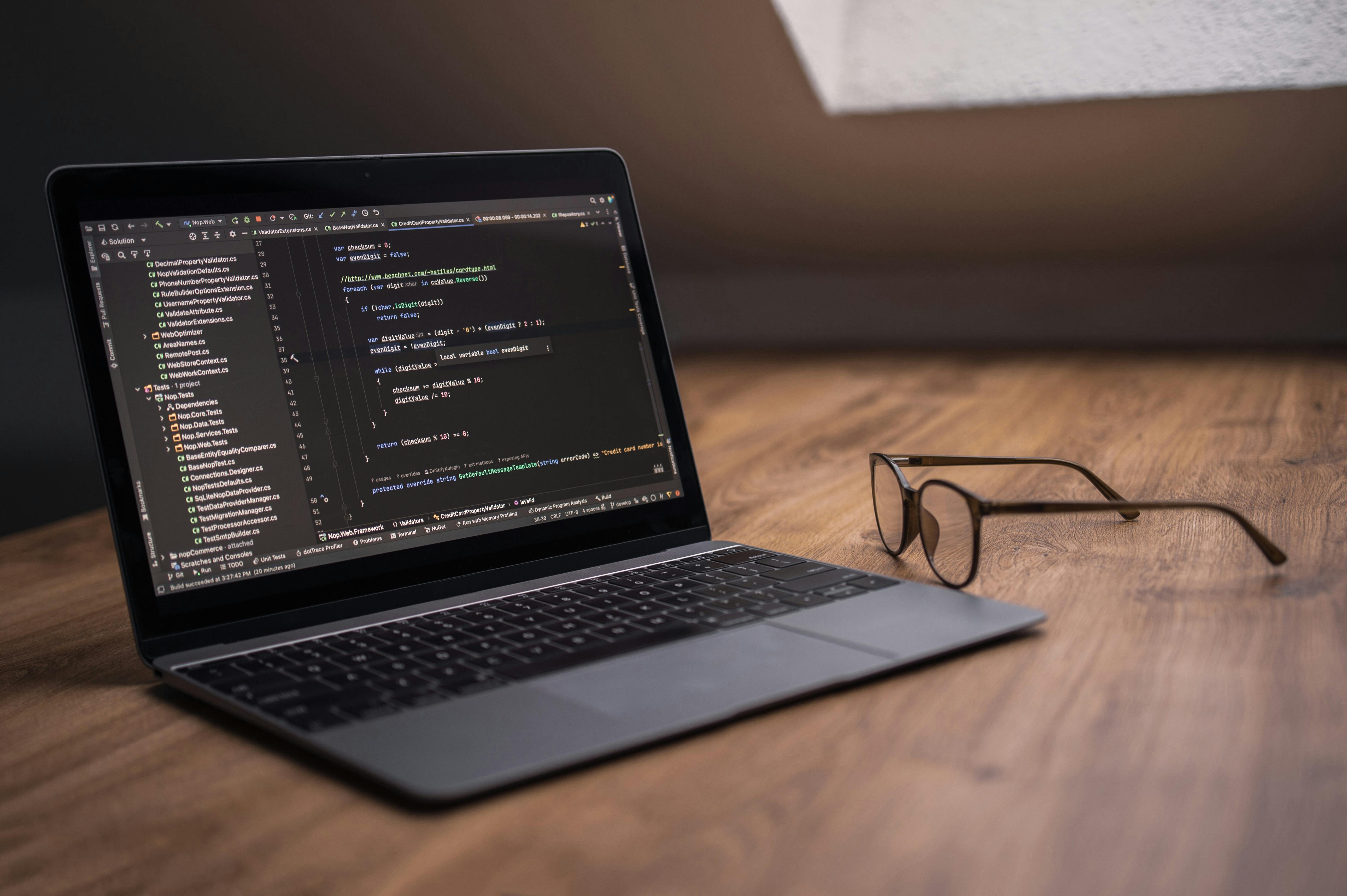 A laptop displaying code editor on a desk next to eyeglasses, ideal for tech themes.