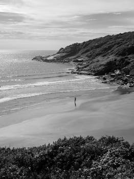 A lone figure walks on a serene Brazilian beach, surrounded by lush landscapes.