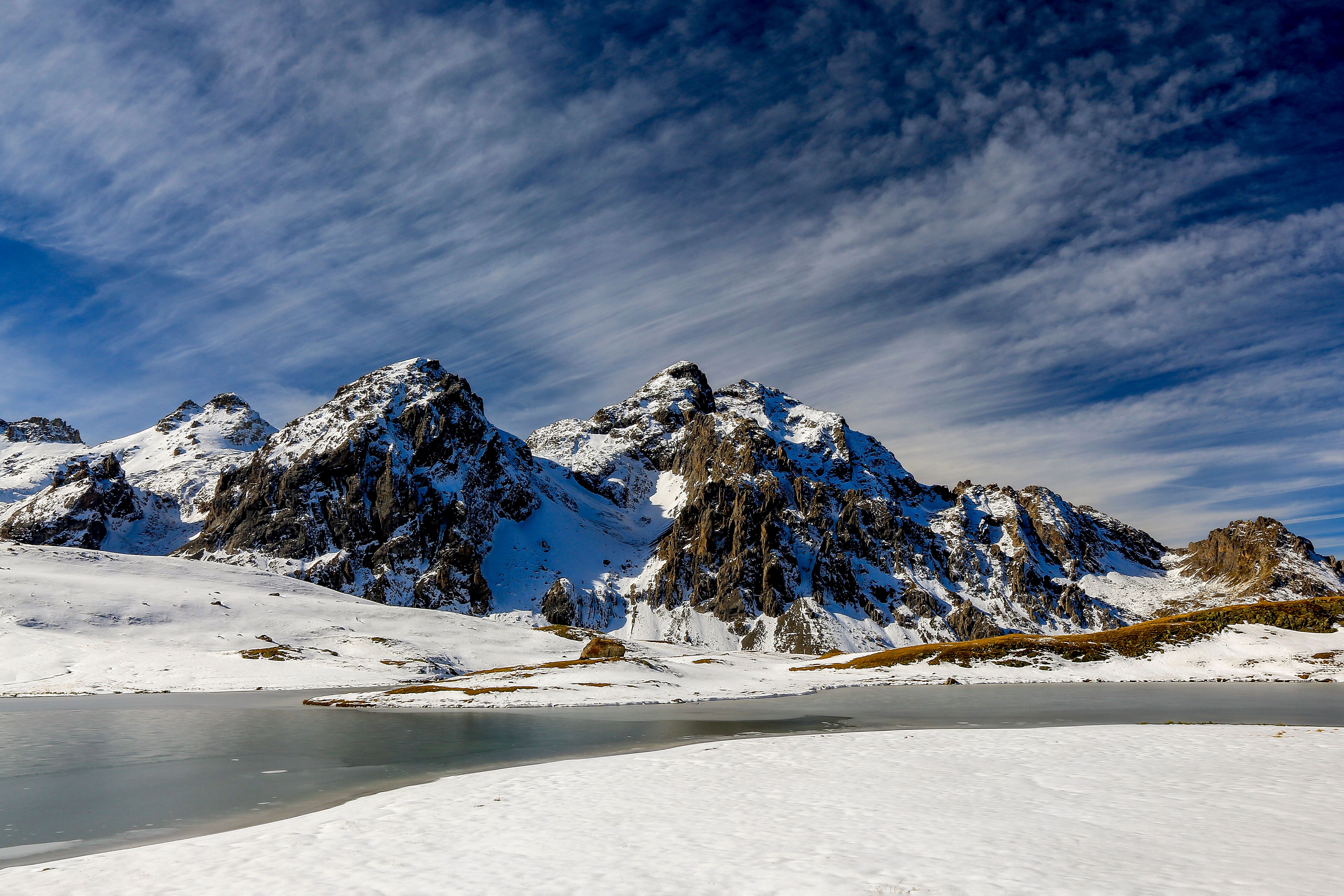 Stunning view of snow-capped mountains and iced lake in Valloire, France under a vibrant blue sky.
