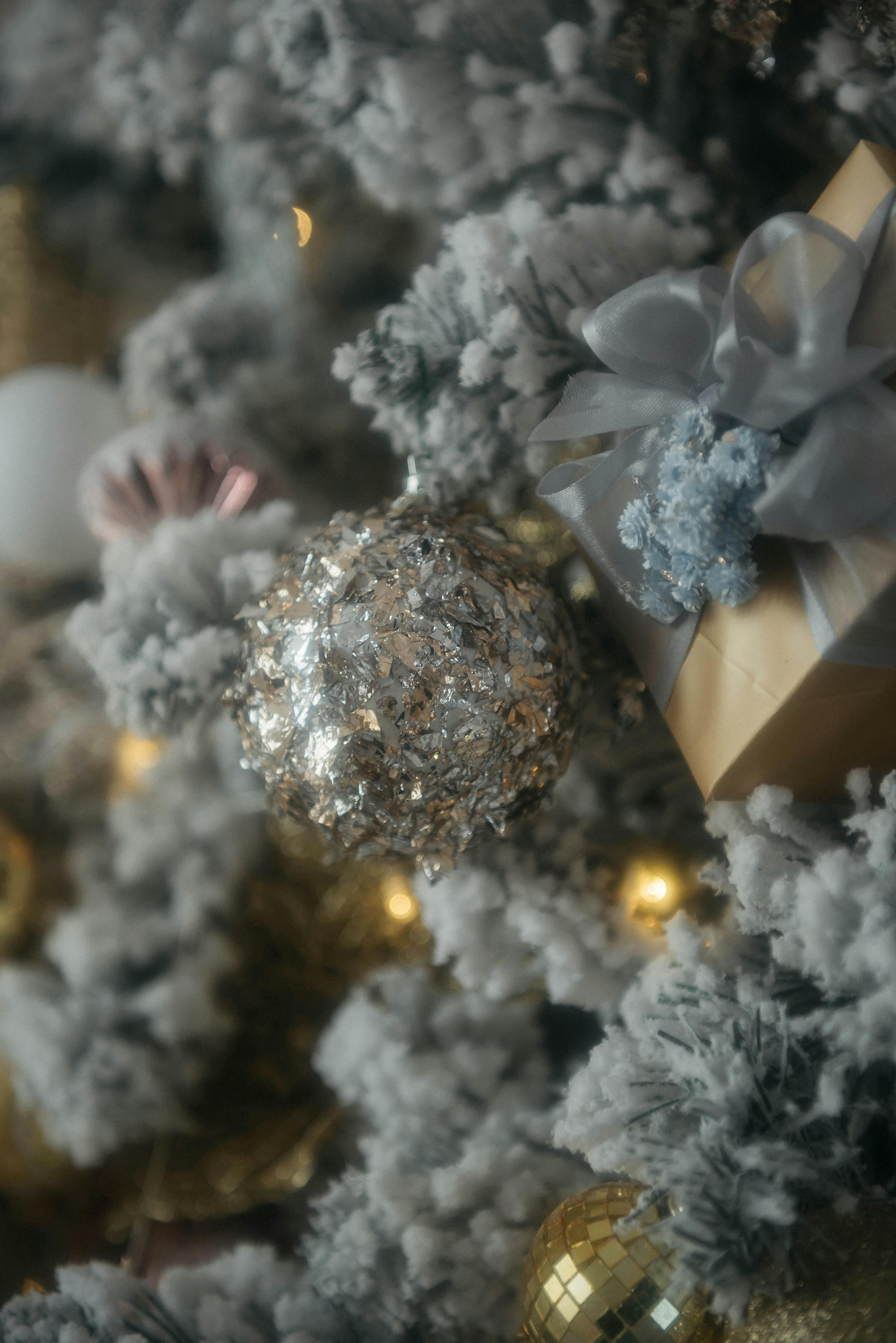Intricate Christmas decor featuring glittering ornaments and wrapped gifts among snow-frosted branches.