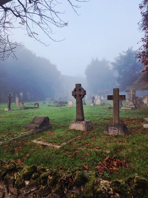 Free A foggy cemetery scene with historic cross gravestones, surrounded by autumn trees. Stock Photo