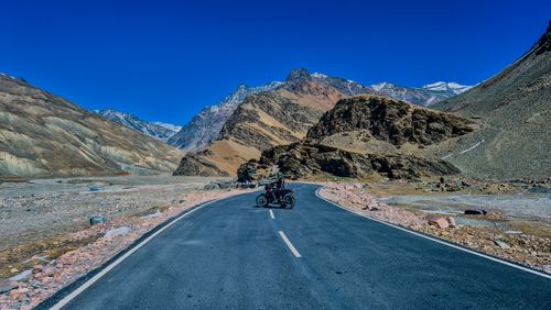 Free A solitary motorcyclist on an open road surrounded by majestic mountains under a clear blue sky. Stock Photo