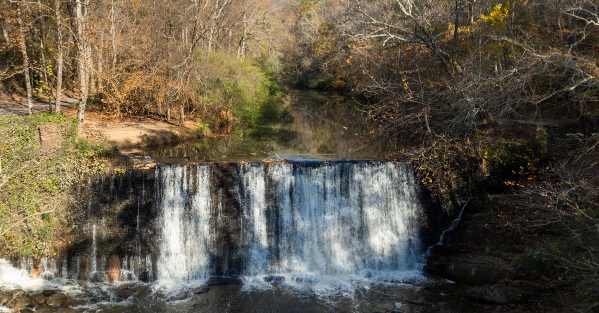 Serene view of Roswell Mill waterfall surrounded by autumn foliage.