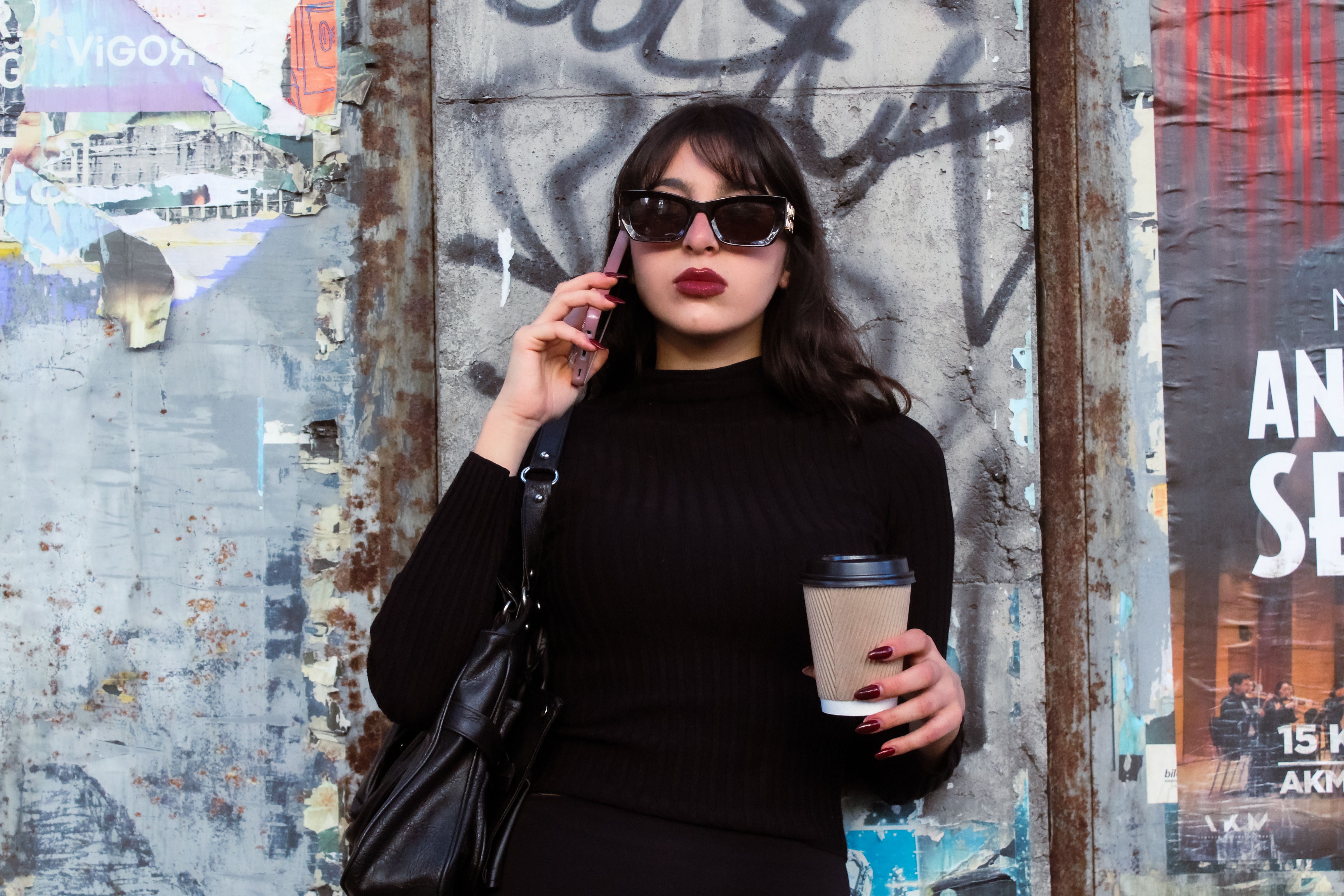Young fashionable woman with coffee and phone in urban street, exuding confidence and style.