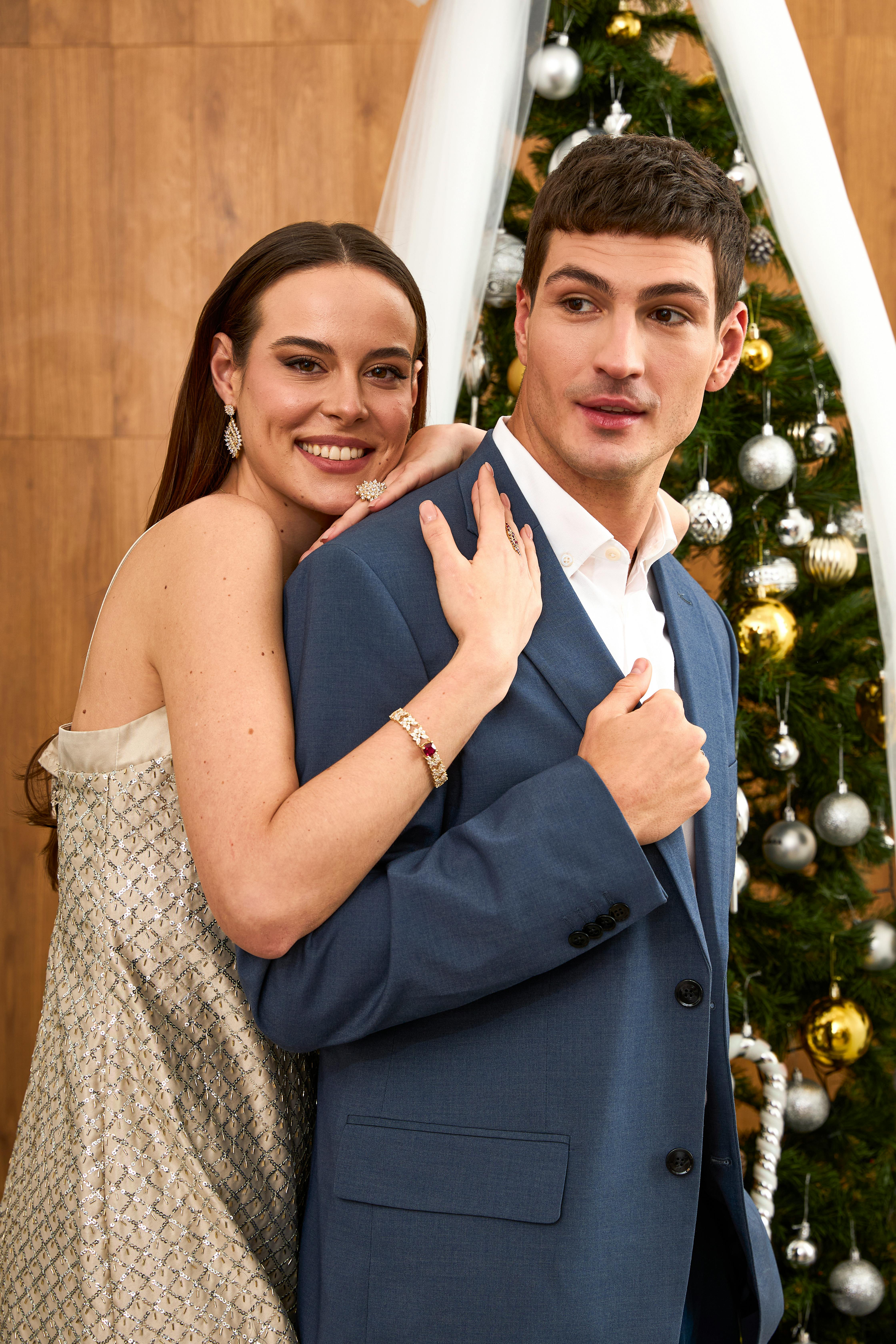 Smiling couple posing elegantly by Christmas tree indoors.