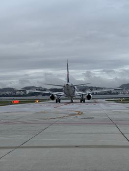 Airplane on runway ready for takeoff against overcast sky.
