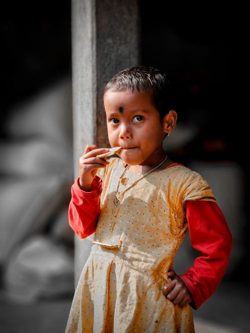 Free A young girl in traditional attire enjoys a snack indoors, captured in a warm, candid moment. Stock Photo