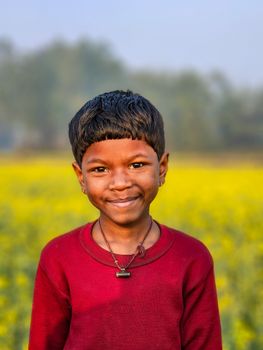 Portrait of a smiling child standing in a vibrant yellow mustard field under clear daylight.