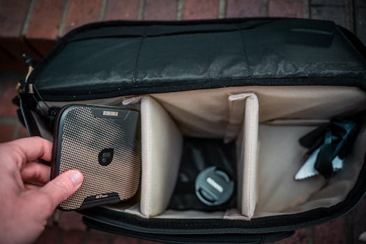 Closeup of a hand placing a portable hard drive into a camera bag. Ideal for tech and travel stock images.