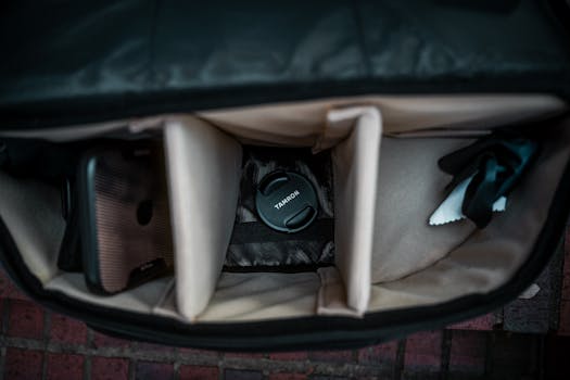 Open camera bag showcasing lens cap, smartphone, and compartments, ideal for photography.
