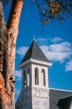 A picturesque church steeple with a slate roof stands tall against a clear blue sky.