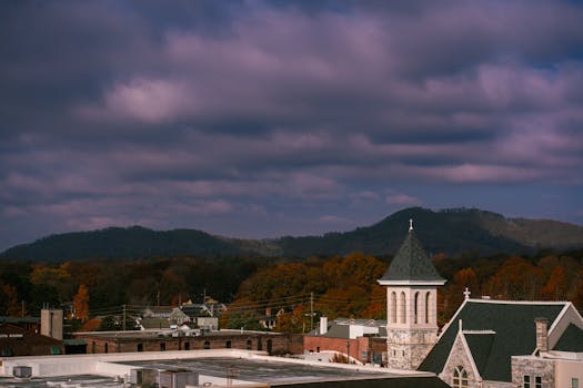 A charming townscape featuring a church tower against a backdrop of autumn mountains and dramatic skies.