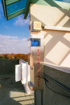 Rooftop emergency call station with exit sign against urban skyline and clear sky.