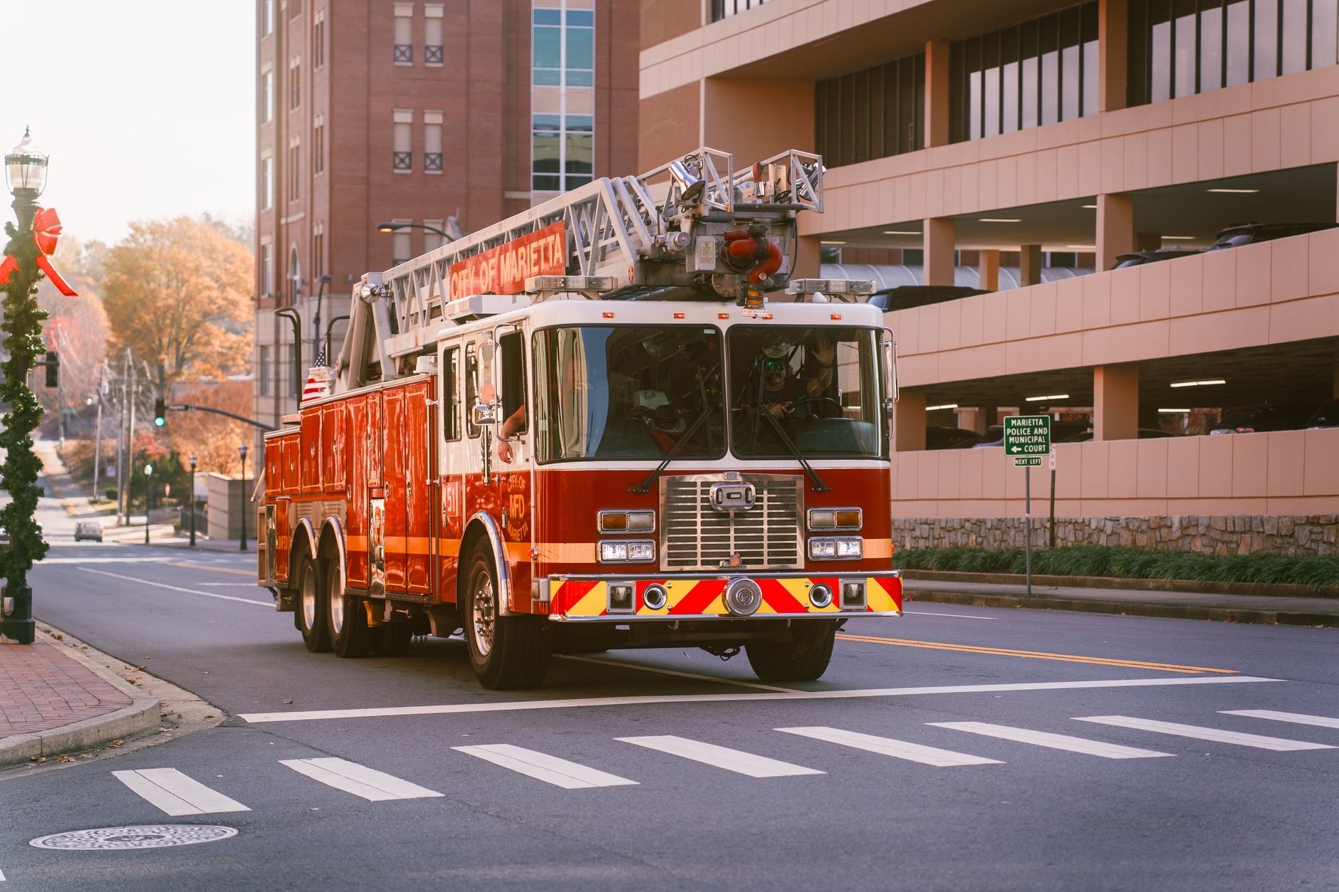 A red fire truck with a ladder drives down a city street in Marietta, showcasing urban readiness.