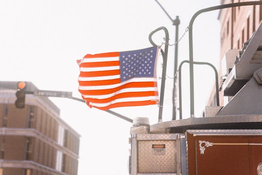 American flag waving on a fire truck in an urban cityscape with buildings.