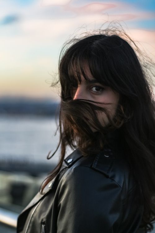 Free Woman with dark hair and leather jacket looking back at sunset by the water. Stock Photo