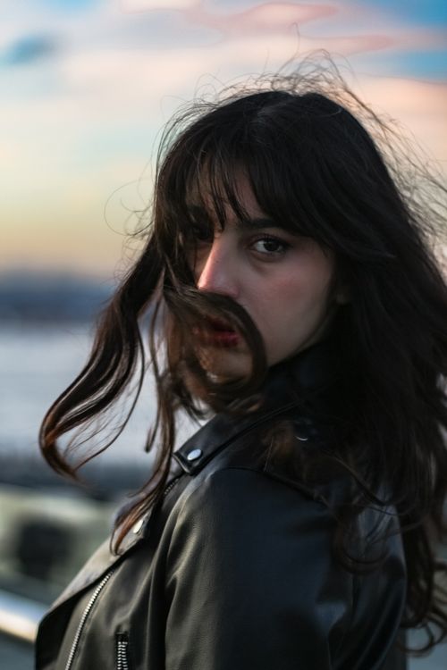 Free Dramatic portrait of a woman wearing a leather jacket, during sunset with flowing hair. Stock Photo