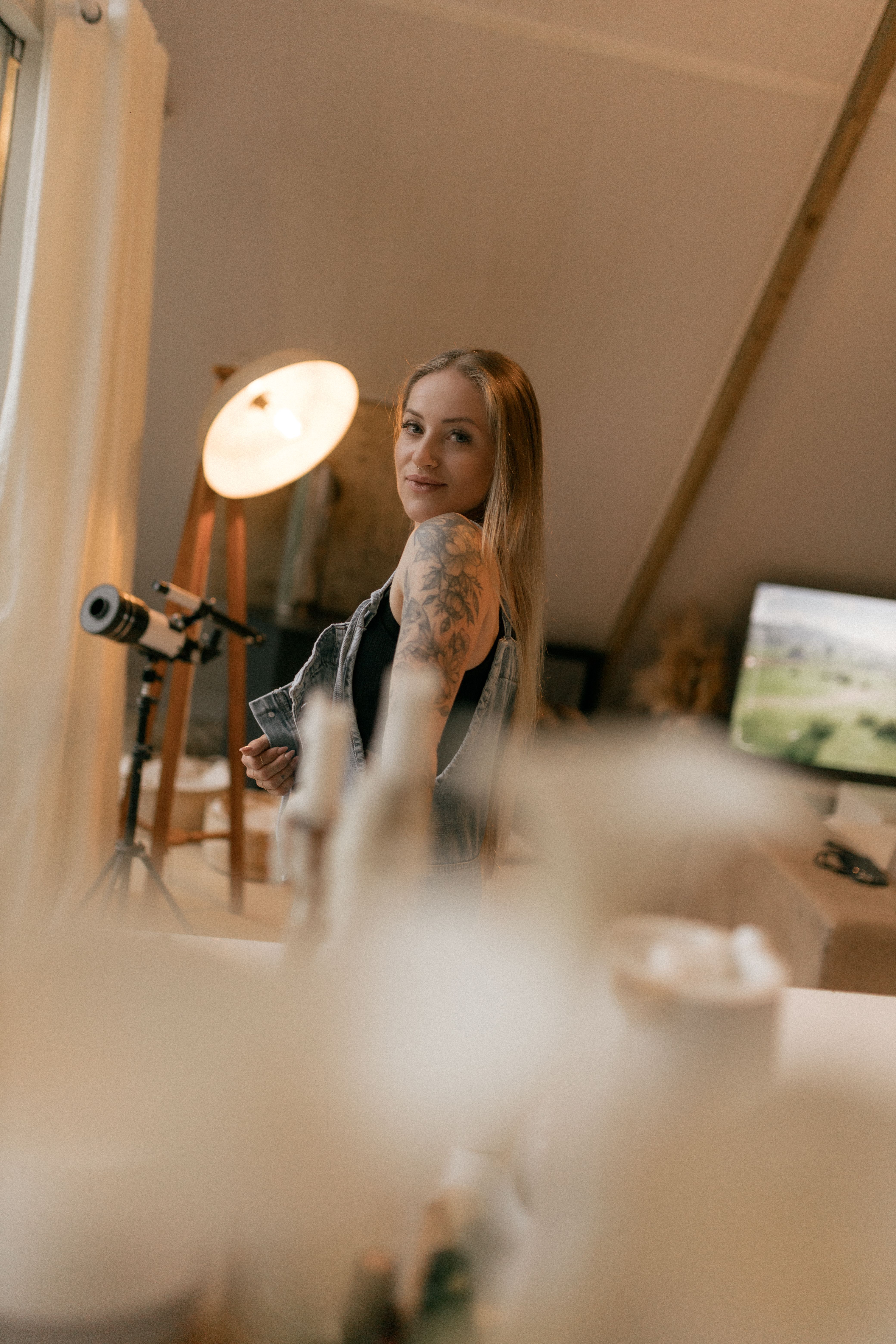 Artistic portrait of a tattooed woman in a cozy studio setting with soft lighting and blurred foreground.