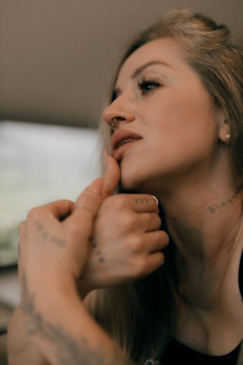 Free Close-up portrait of a young woman deep in thought, showcasing tattoos and a nose piercing, with a blurred indoor background. Stock Photo
