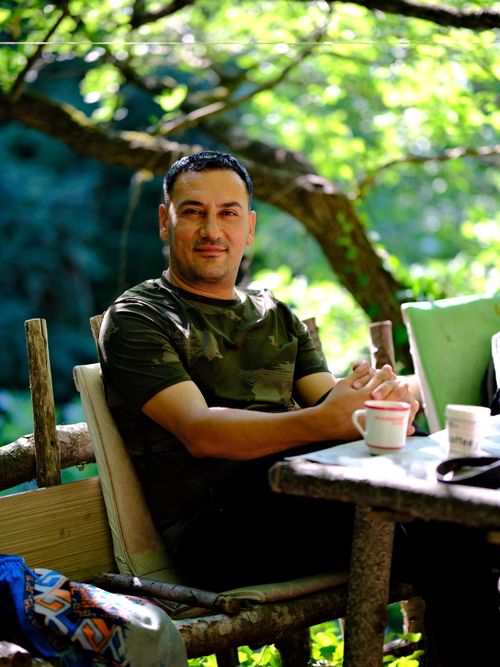 Free Man in camo shirt enjoying coffee at outdoor table surrounded by greenery. Stock Photo
