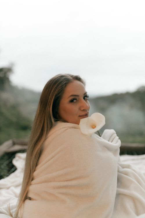 Free A serene outdoor portrait of a woman wrapped in a blanket with a calla lily, in a natural setting. Stock Photo