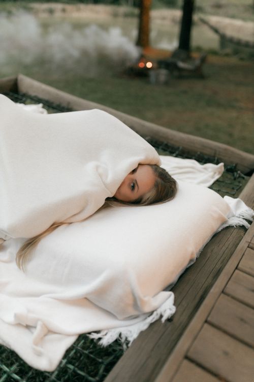 Free A person wrapped in a blanket resting outdoors near a campfire. Stock Photo