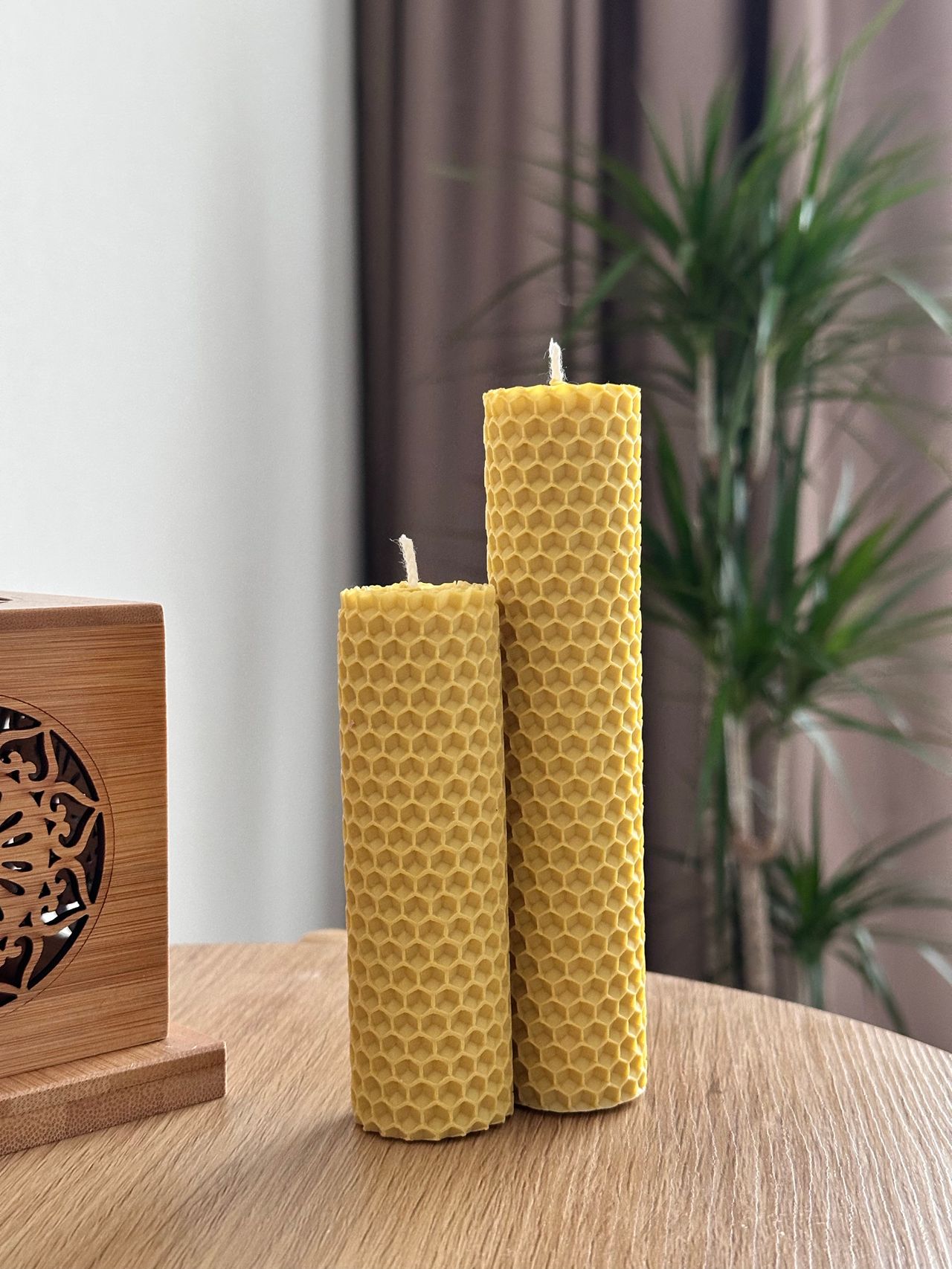 Two tall honeycomb-textured beeswax candles on a wooden table