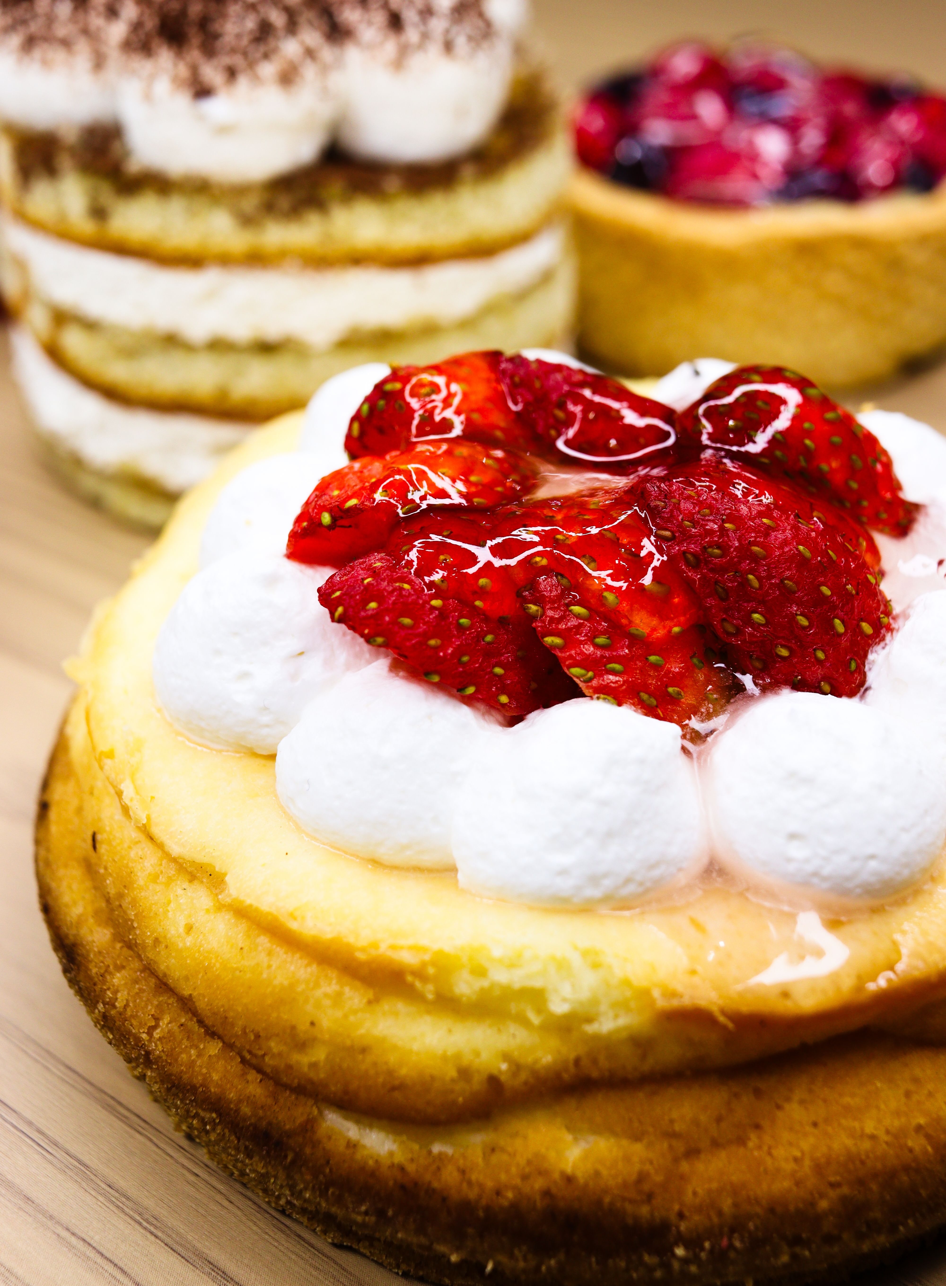 Close-up of various cakes including strawberry cheesecake with whipped cream and fresh strawberries.