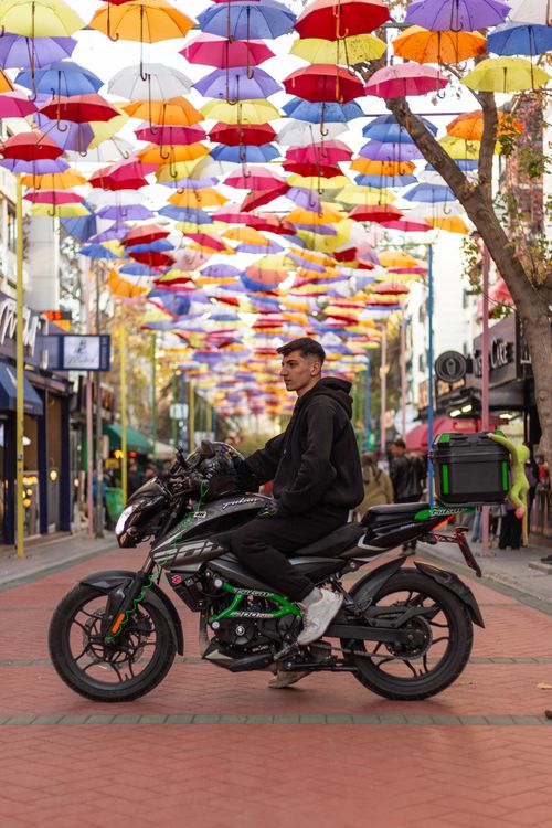 Free A motorcyclist poses on a street with colorful umbrellas overhead in Ankara. Stock Photo