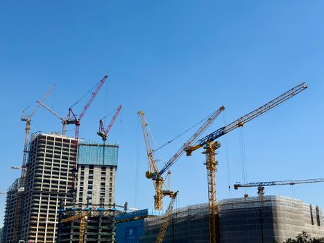 Tower cranes at a skyscraper construction site under a clear blue sky.