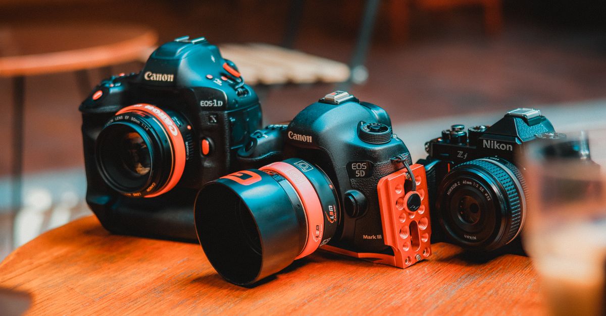 Three professional DSLR cameras displayed on a wooden surface in a warm setting.