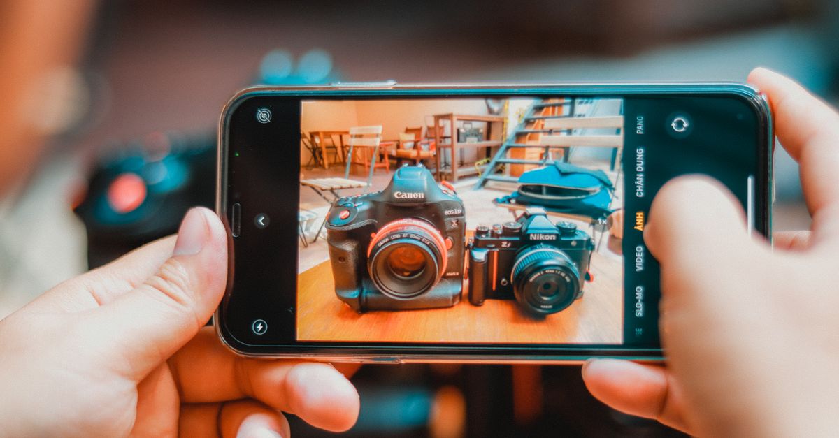 Person photographing DSLR and vintage cameras with smartphone indoors.