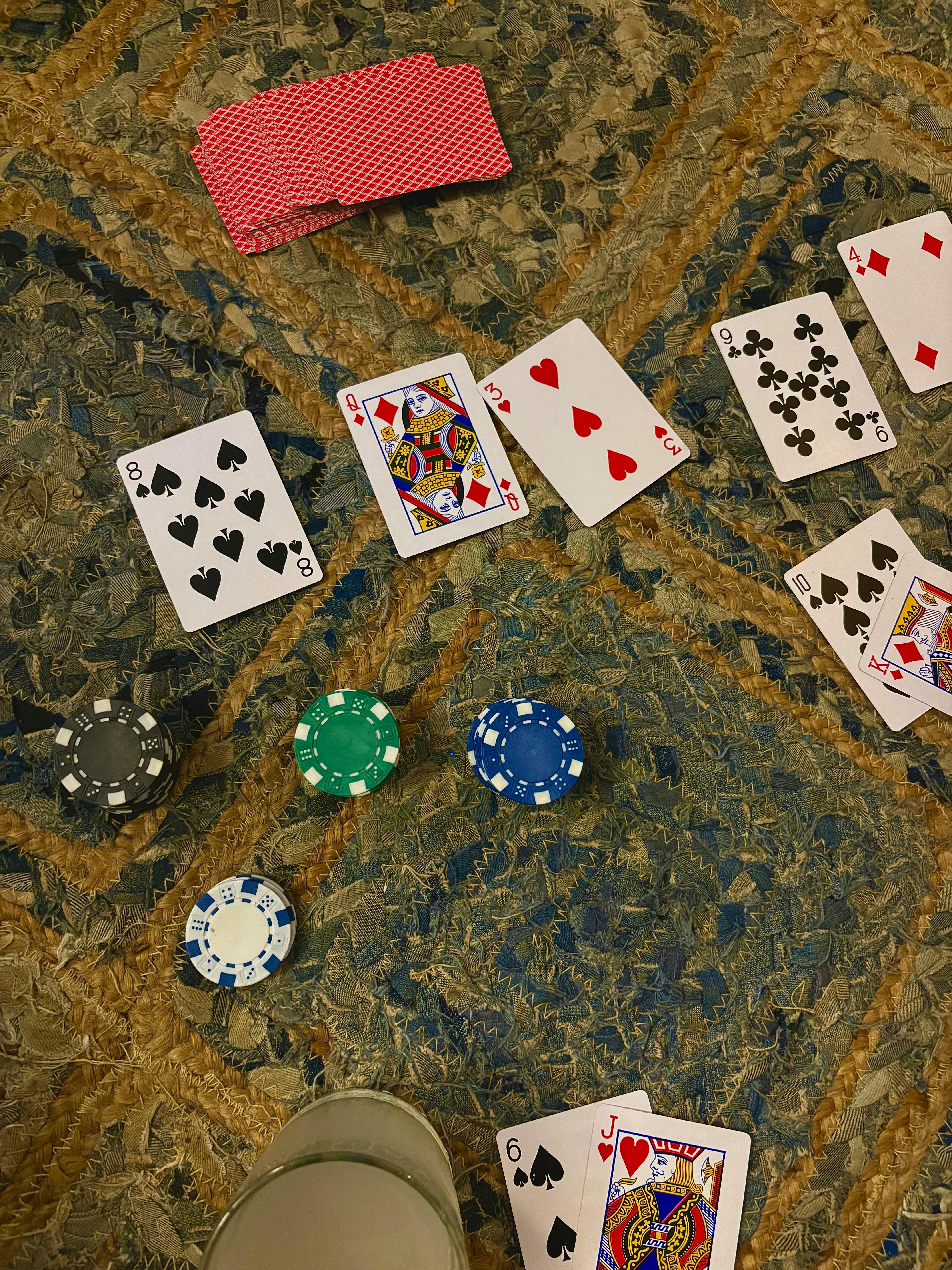 Top view of a poker game scene with scattered playing cards and chips on a patterned carpet.