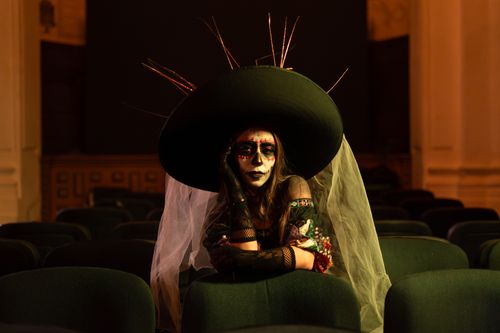 Free Woman in Day of the Dead makeup sitting in a dim theater, evoking a dramatic feel. Stock Photo