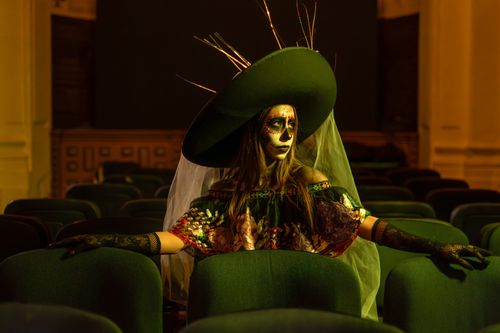 Free Woman in elaborate Day of the Dead costume and makeup sitting in empty auditorium. Stock Photo
