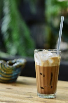 Refreshing iced coffee with cream served in a glass with ice and straw, on a rustic wooden table.