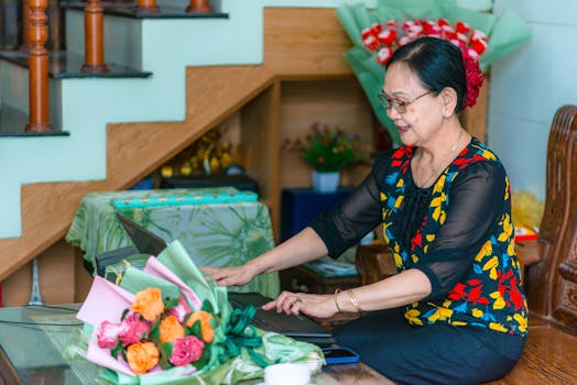 Senior woman enjoying time with a laptop at home, surrounded by flowers, creating a warm and inviting atmosphere.