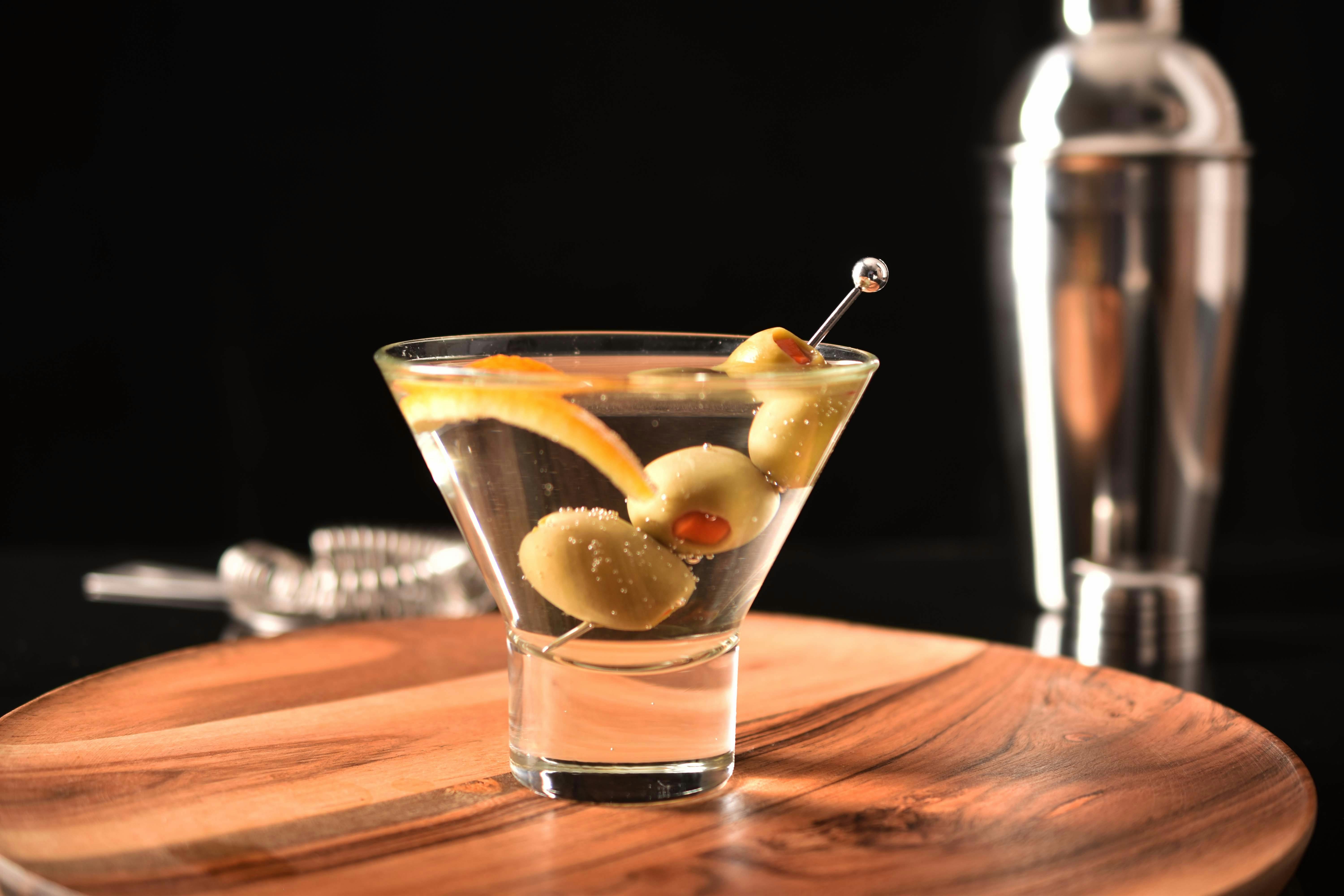 Elegant martini cocktail with olives, garnished on a wooden tray, perfect for cocktail hour.