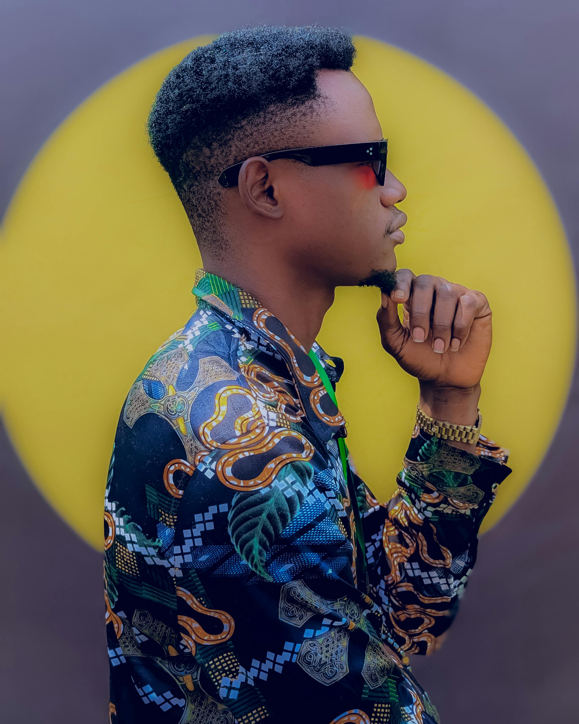 A man in colorful attire poses thoughtfully against a vivid circular backdrop.