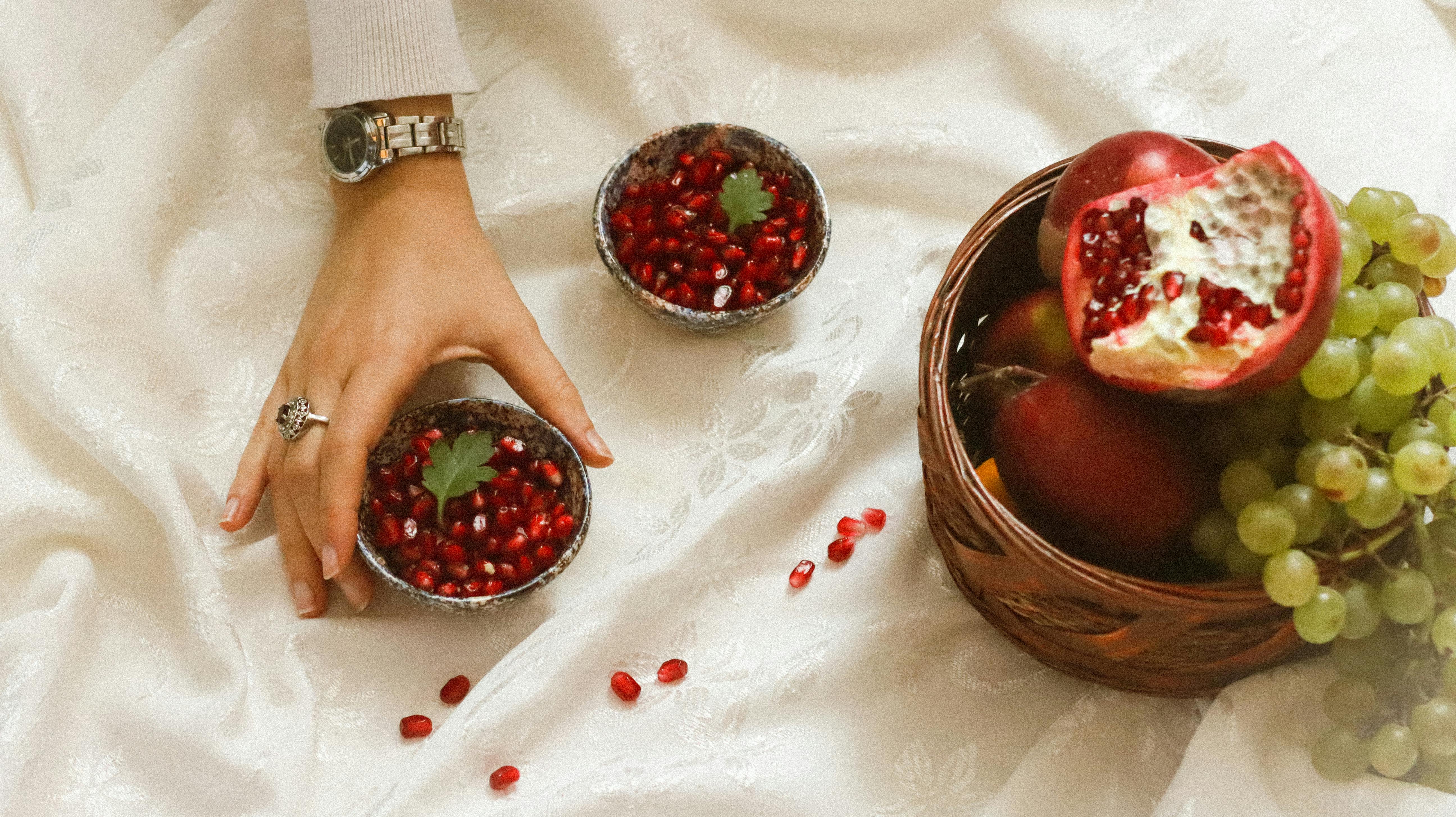 Elegant composition of pomegranate seeds, apples, grapes, and hand on a soft fabric.